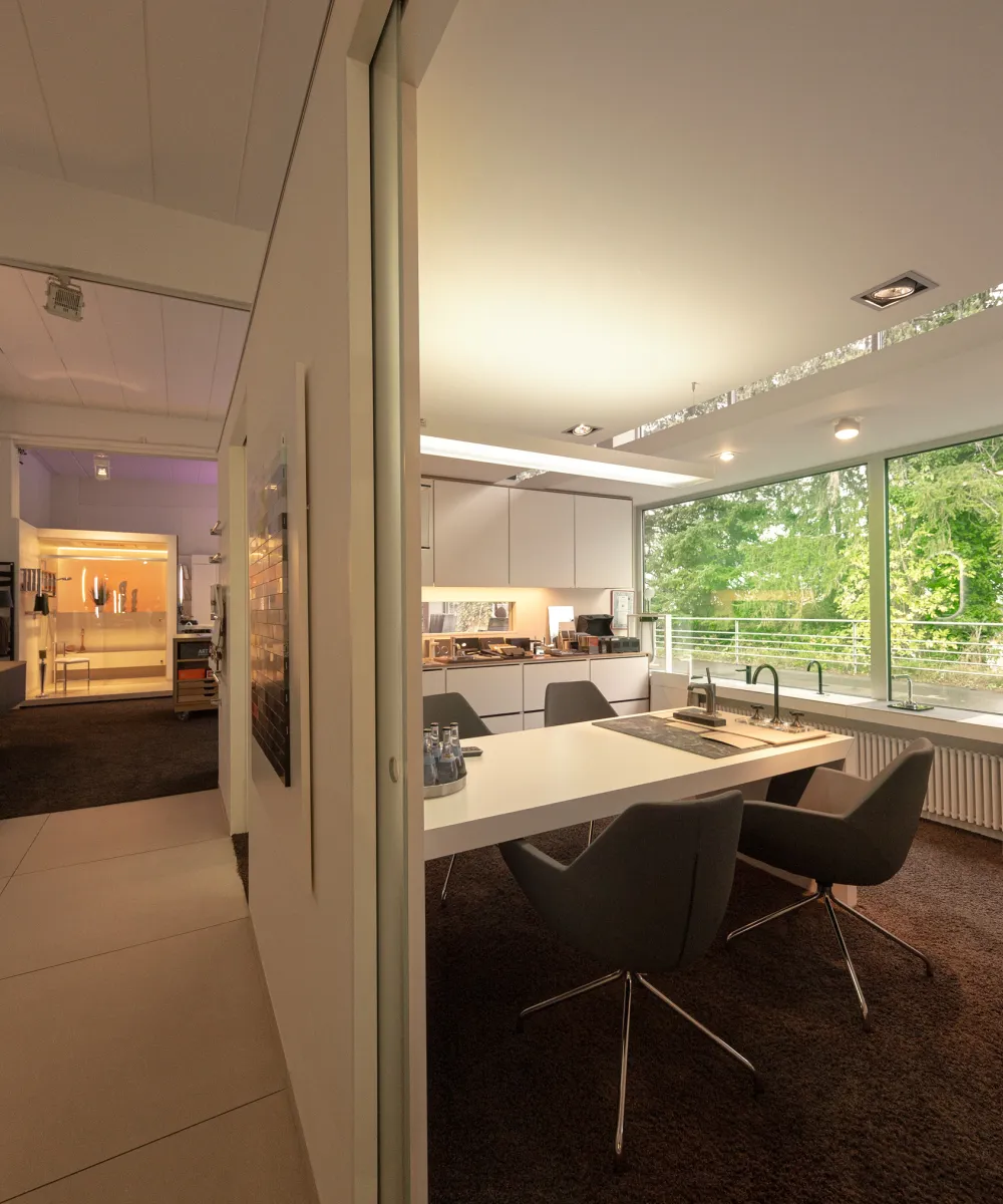 Ein modernes Badstudio mit groĂen Fensterfronten, die viel natĂŒrliches Licht in den Raum lassen und den Blick auf grĂŒne BĂ€ume freigeben.